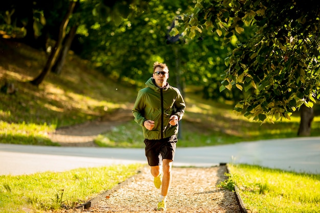 Jovem bonito e atlético correndo enquanto faz exercícios no parque verde ensolarado