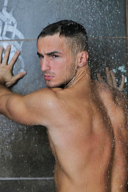jovem bonito e atraente com corpo musculoso molhado tomando banho no banho com azulejos pretos no fundo