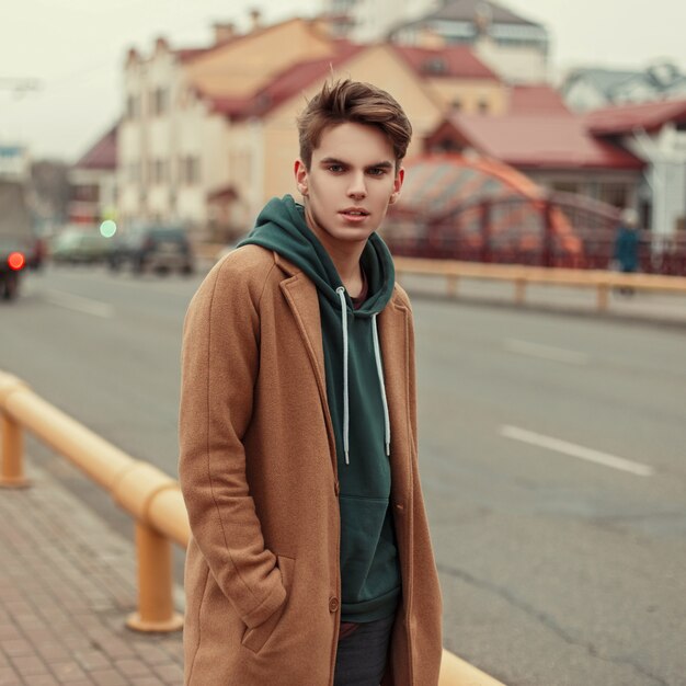 Jovem bonito e elegante em um casaco retrô da moda com capuz na rua