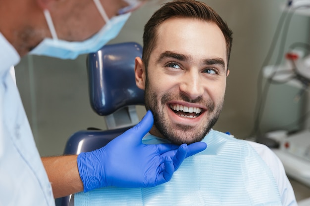 Jovem bonito e feliz sentado no centro médico dentista