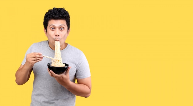 Jovem bonito e moderno homem asiático comendo macarrão instantâneo gostoso quente e picante usando pauzinhos e tigela