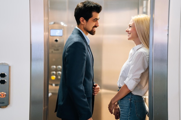 Foto jovem bonito e mulher bonita olhando um ao outro sorrindo em pé dentro do elevador no shopping. casal de negócios alegre reunião no elevador do prédio de escritórios moderno.