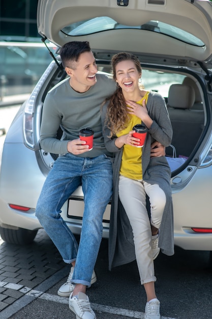 Jovem bonito e mulher tomando café perto de um carro