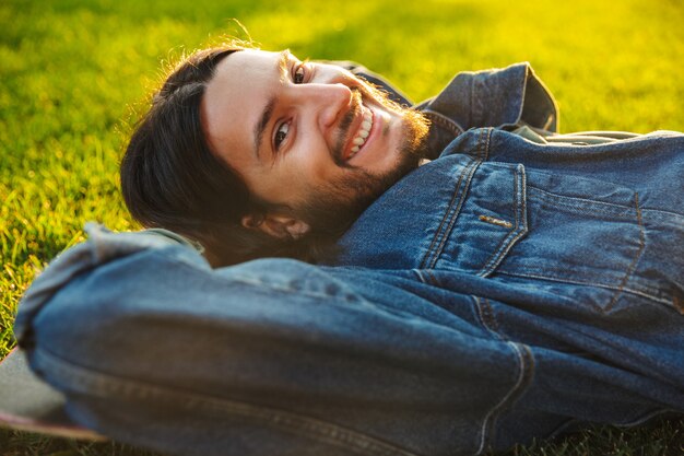 Jovem bonito e sorridente passando um tempo no parque, deitado em um skate