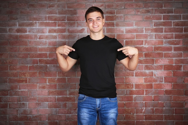 Foto jovem bonito em camiseta preta em branco em pé contra a parede de tijolos