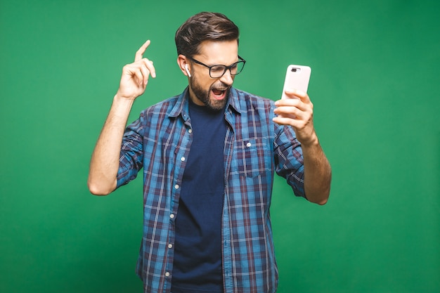 Jovem bonito em fones de ouvido, mantendo os olhos fechados enquanto dança. sobre fundo verde. isolado.