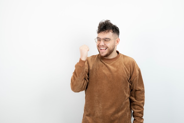 jovem bonito em pé e se sentindo feliz com uma parede branca.