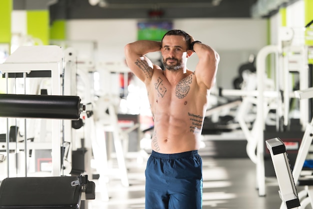 Jovem bonito em pé forte na academia e flexionando os músculos Muscular Atlético Fisiculturista Modelo de fitness posando após exercícios