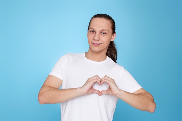 Jovem bonito em t-shirt branca mostrando amor coração gesto isolado sobre fundo azul. Emoções humanas, expressões faciais