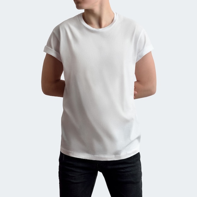 Jovem bonito em t-shirt em branco e calças escuras em um fundo branco de estúdio em branco. Pose frontal com os braços para trás. O maquete pode ser usado em sua vitrine.