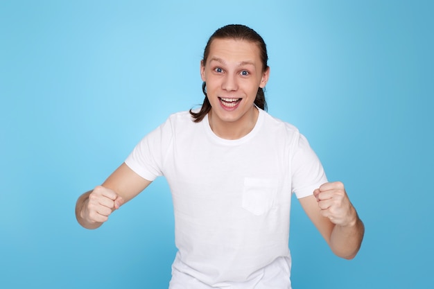 Jovem bonito em t-shirt mostrando o gesto de vitória isolado sobre fundo azul.