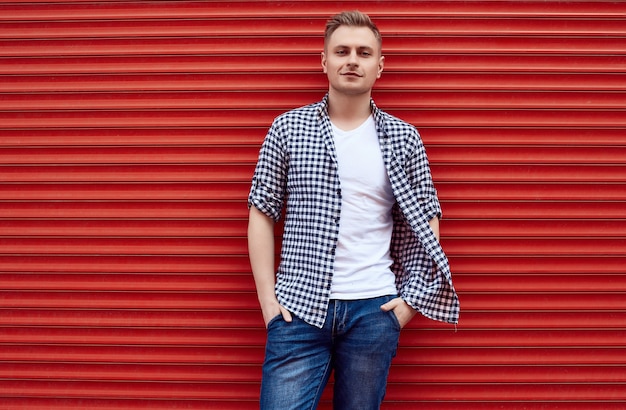 Jovem bonito em uma camisa e calça jeans perto do portão vermelho