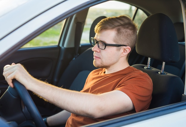 Jovem bonito em uma camiseta marrom, dirigindo um carro.