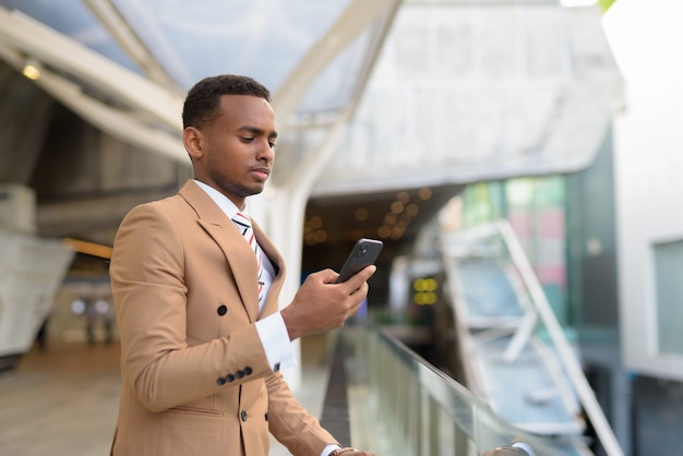 Jovem bonito empresário africano usando telefone em uma passarela na cidade