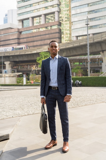 Jovem bonito empresário feliz de terno segurando mala nas ruas da cidade ao ar livre