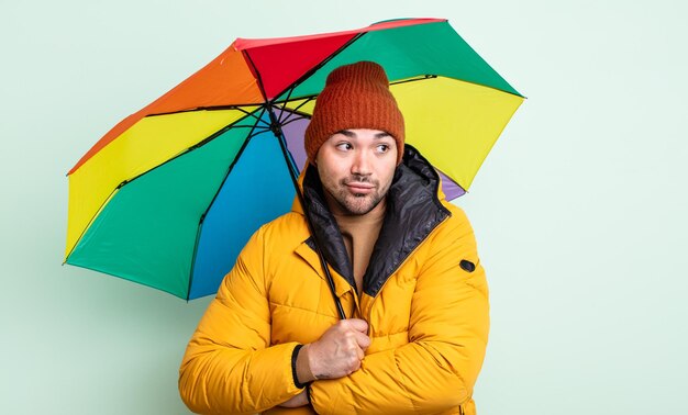 Jovem bonito encolhendo os ombros, sentindo-se confuso e incerto. conceito de chuva e guarda-chuva