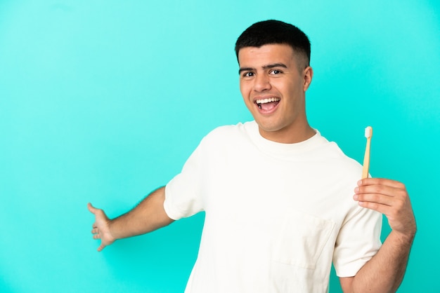 Jovem bonito escovando os dentes na parede azul isolada, estendendo as mãos para o lado e convidando-o a vir