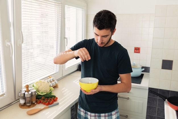 Jovem bonito está tomando café na cozinha em casa.