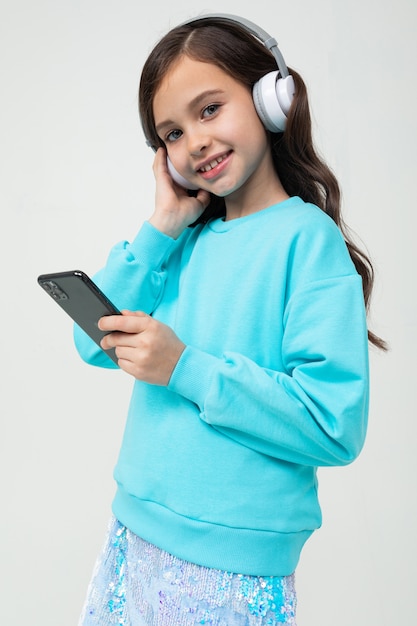 Jovem bonito Europeu em uma blusa azul gosta de música em grandes fones de ouvido elegantes com um telefone nas mãos em um estúdio de tons claros