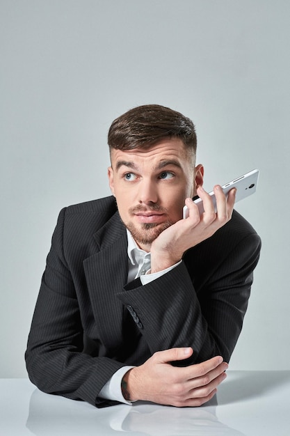 Jovem bonito falando ao telefone enquanto está sentado em seu local de trabalho no escritório