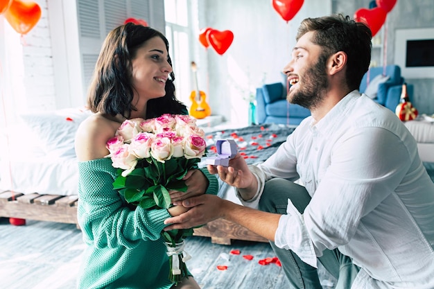 Jovem bonito faz uma proposta para sua linda namorada se casar com ele em um lindo quarto com um fundo romântico. Marido e esposa