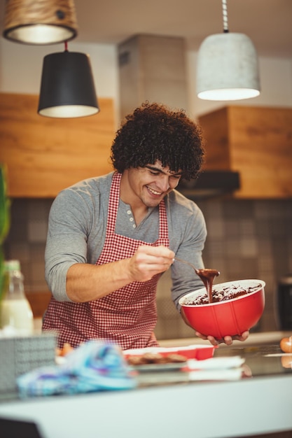 Foto jovem bonito fazendo biscoitos em sua cozinha para seus amigos. ele está despejando massa de chocolate em moldes.