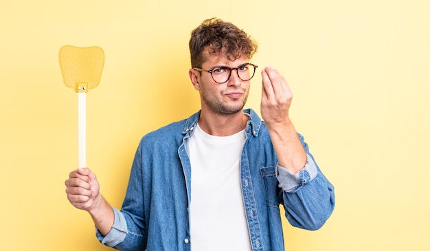 Jovem bonito fazendo capice ou gesto de dinheiro, dizendo para você pagar. conceito flyswatter