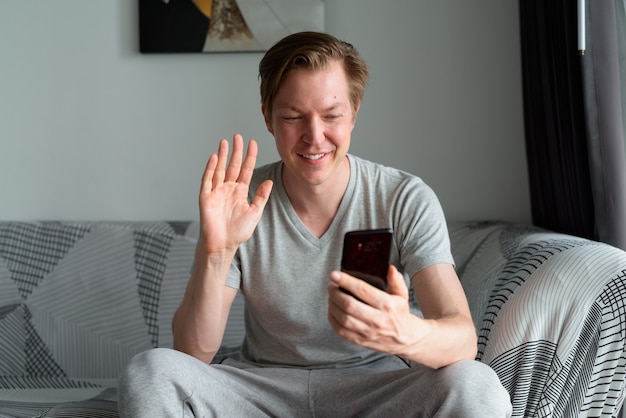 Jovem bonito feliz com videochamada com o telefone em casa