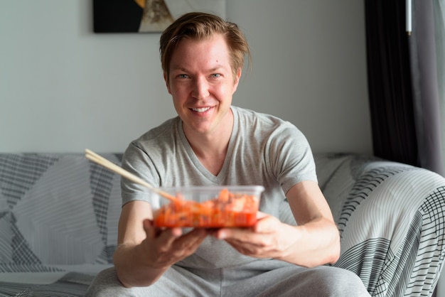 Jovem bonito feliz dando kimchi na sala de estar de casa