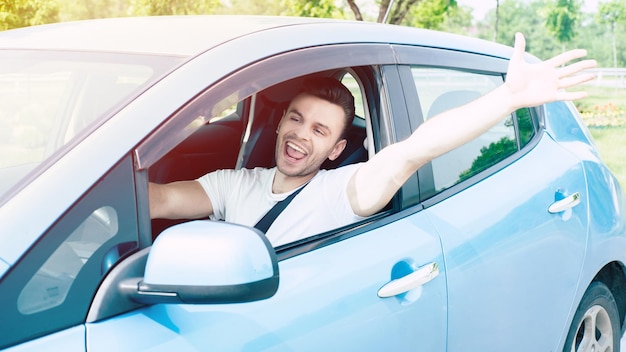 Jovem bonito feliz dirigindo seu carro e sorrindo. Motorista animado na cidade urbana. Carro elétrico, veículo do futuro