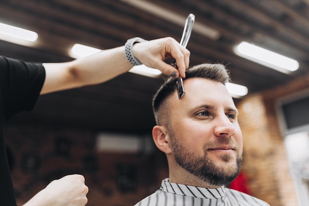 Jovem bonito feliz visitando o cabeleireiro em um salão de barbearia