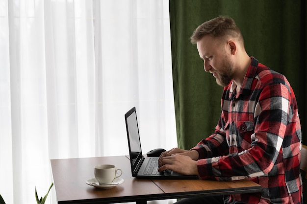 jovem bonito freelancer usando laptop trabalhando em casa estudando on-line cara digitando em PC laptop navegando na internet olhando para a tela desfrutando de trabalho remoto sentado à mesa