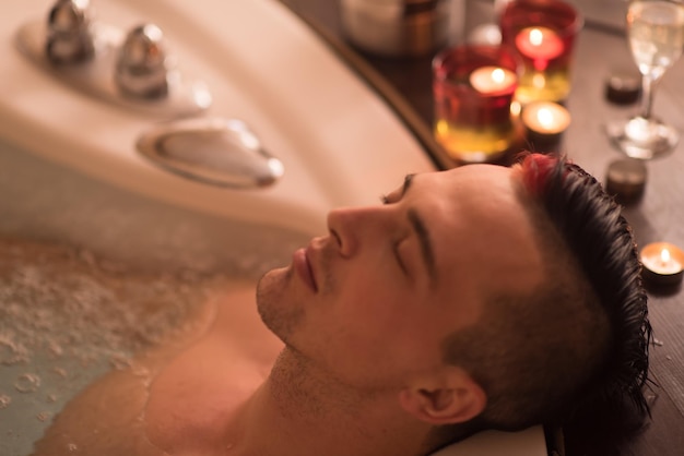 jovem bonito gosta de relaxar no jacuzzi com velas e champanhe no spa resort de luxo