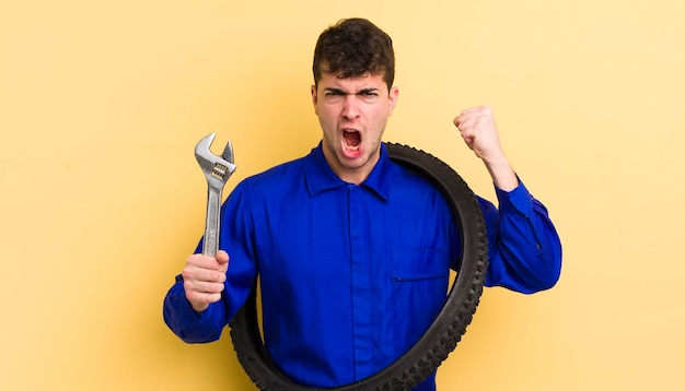 Jovem bonito gritando agressivamente com um conceito de reparador de bicicleta de expressão de raiva