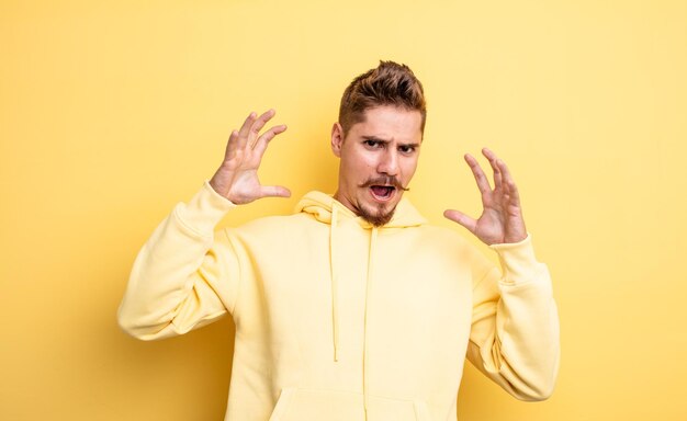 Jovem bonito gritando com as mãos no ar, sentindo-se furioso, frustrado, estressado e chateado. conceito de bigode estranho