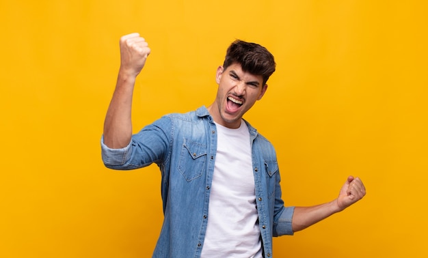 Jovem bonito gritando triunfantemente, parecendo um vencedor animado, feliz e surpreso, comemorando