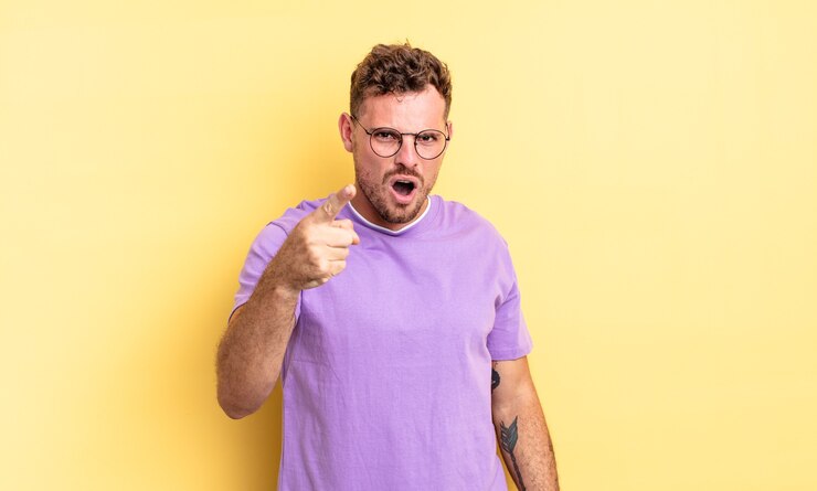Foto jovem bonito hispânico apontando para a câmera com uma expressão agressiva e zangada, parecendo um chefe louco e furioso