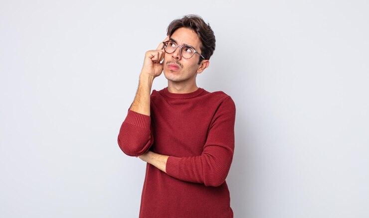 Foto jovem bonito hispânico com um olhar concentrado, pensando com uma expressão duvidosa, olhando para cima e para o lado
