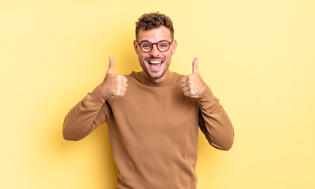 Jovem bonito hispânico sorrindo, parecendo feliz, positivo, confiante e bem-sucedido, com os dois polegares para cima