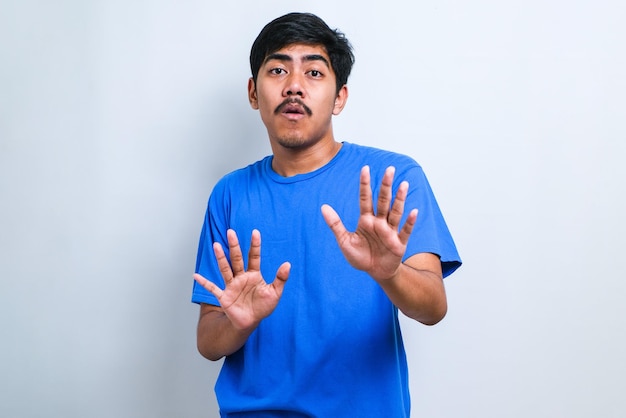 Jovem bonito homem asiático vestindo t-hirt casual em pé sobre fundo branco Afastando as palmas das mãos mostrando recusa e negação com expressão de medo e nojenta. Pare e proibido.