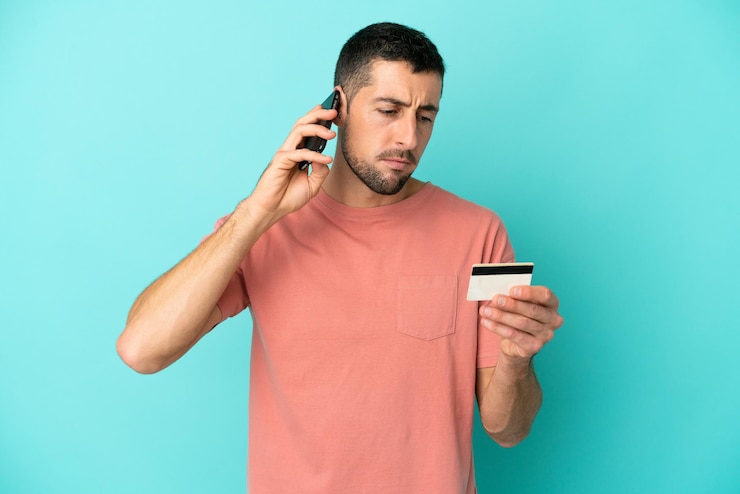 Foto jovem bonito homem caucasiano isolado em um fundo azul, comprando com o celular com um cartão de crédito
