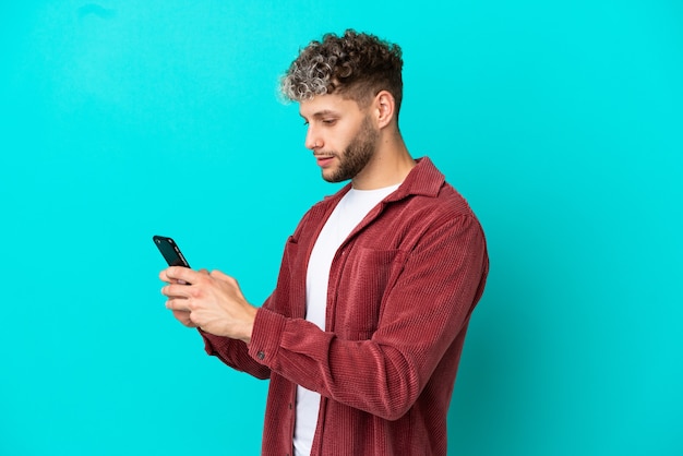 Jovem bonito homem caucasiano isolado em um fundo azul enviando uma mensagem ou e-mail com o celular