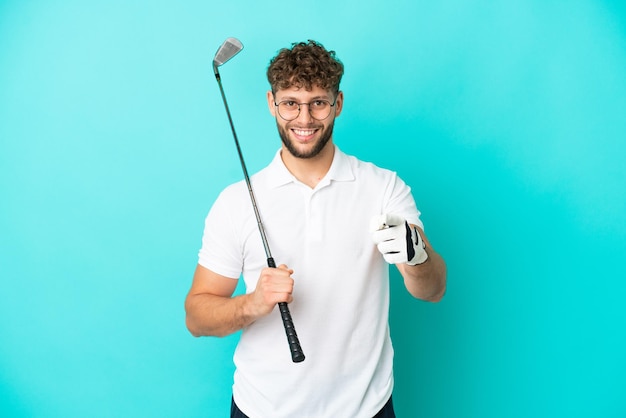 Jovem bonito homem caucasiano isolado em um fundo azul jogando golfe e apontando para a frente