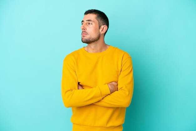 Jovem bonito homem caucasiano isolado em um fundo azul, mantendo os braços cruzados