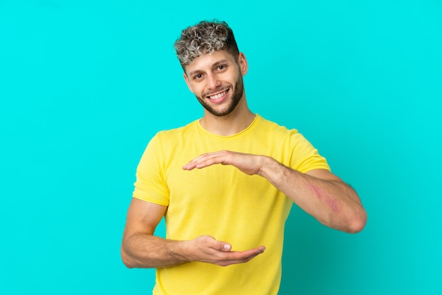 Jovem bonito homem caucasiano isolado em um fundo azul segurando copyspace imaginário na palma para inserir um anúncio