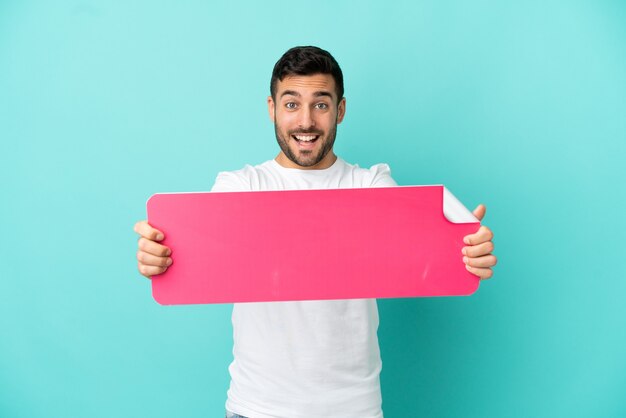 Jovem bonito homem caucasiano isolado em um fundo azul segurando um cartaz vazio