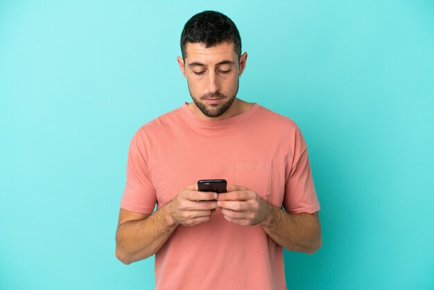 Jovem bonito homem caucasiano isolado em um fundo azul usando telefone celular