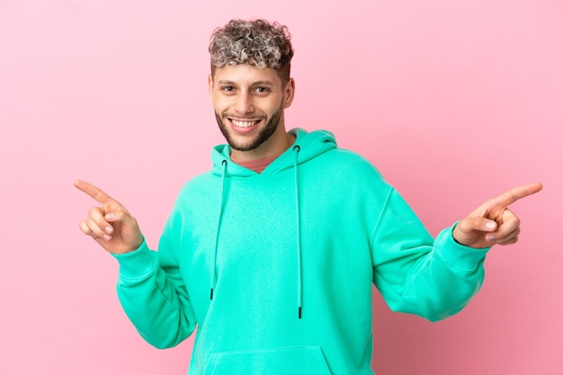 Jovem bonito homem caucasiano isolado em um fundo rosa apontando o dedo para as laterais e feliz