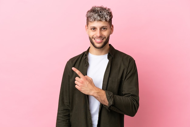 Jovem bonito homem caucasiano isolado em um fundo rosa apontando para o lado para apresentar um produto