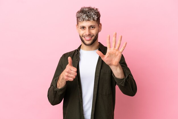 Jovem bonito homem caucasiano isolado em um fundo rosa contando seis com os dedos